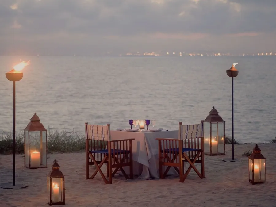 A table for two on the sand at dusk, lit by lanterns